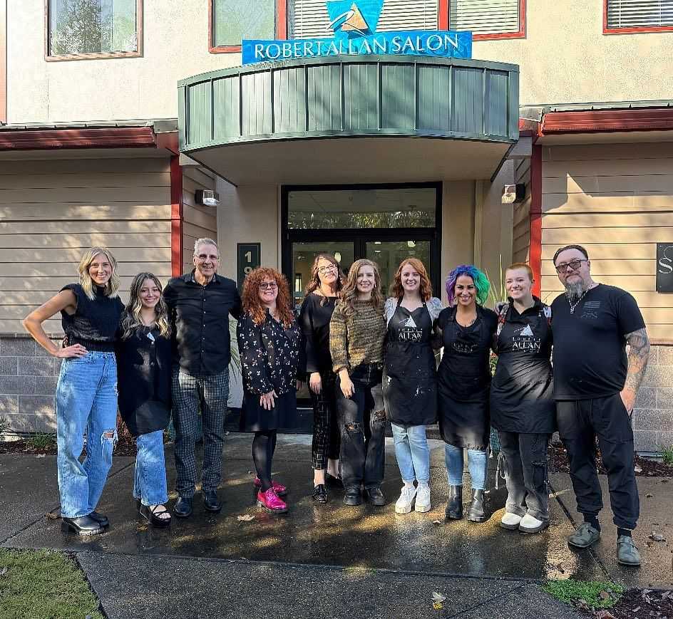 Group of nine smiling people standing in front of Robert Allan Salon.