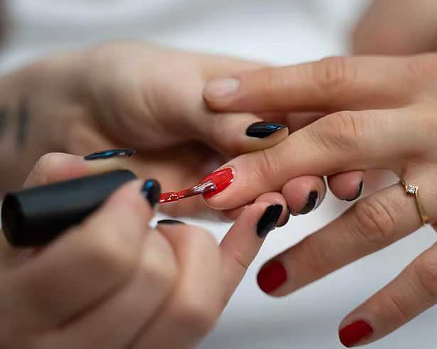 Close-up of hands applying red nail polish during a manicure session.